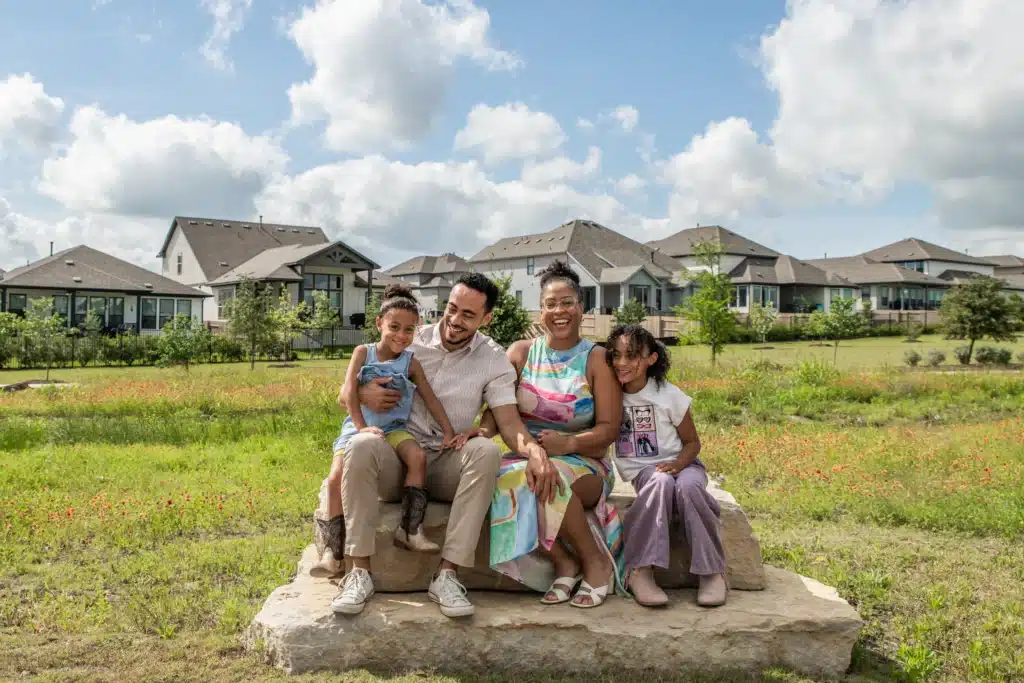 A young family of four sit smiling in front of new construction homes in Easton Park.